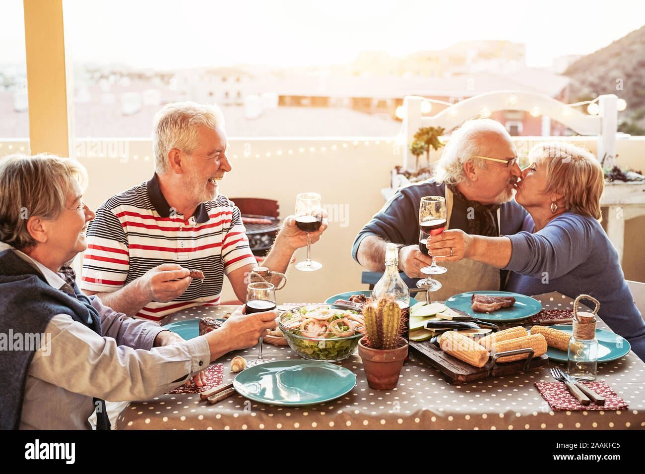 Happy senior friends dining and cheering with red wine at barbecue in terrace outdoor - Retired people having fun at bbq party on patio Stock Photo