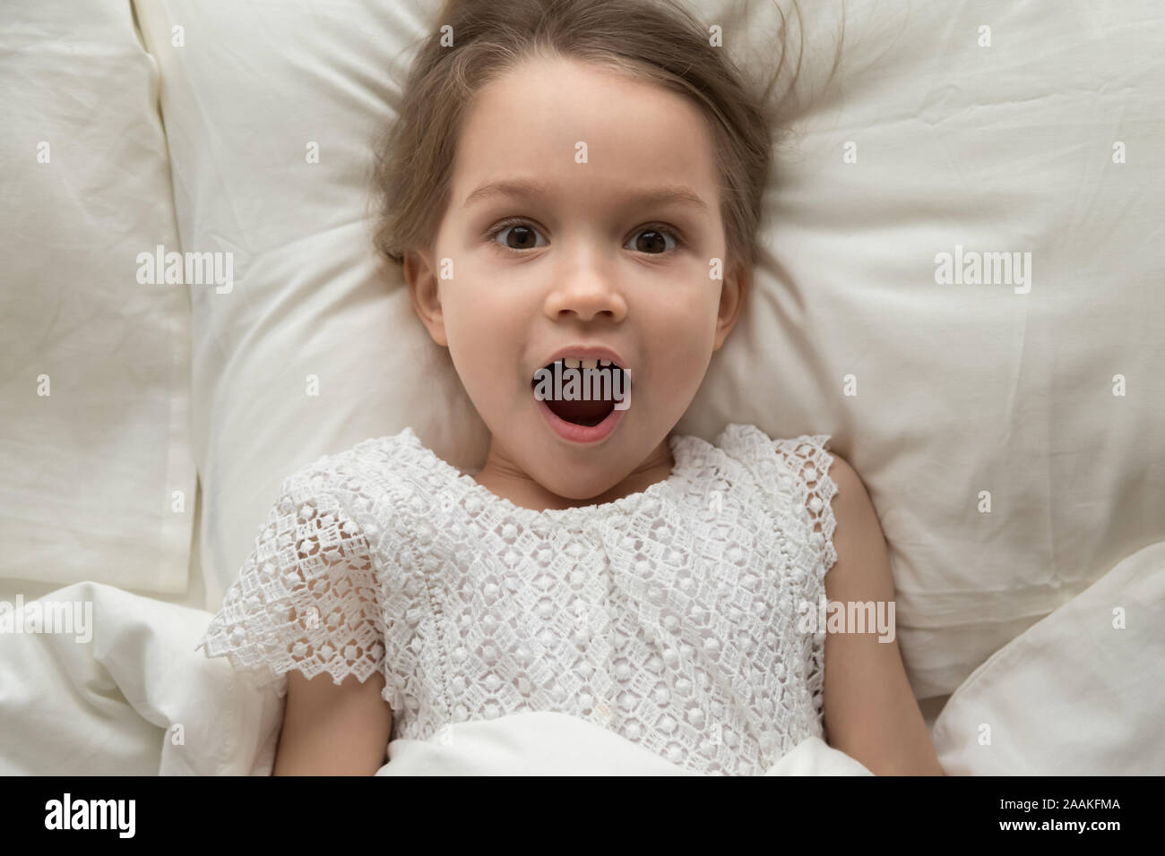 Top view of little girl lying in bed feel surprised Stock Photo