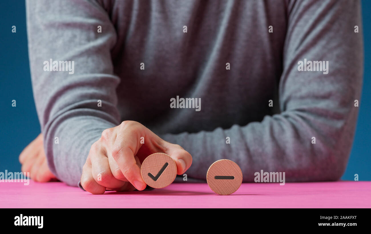 Male hand holding a wooden cut circle with check mark on it with another circle with minus sign in a conceptual image. Stock Photo