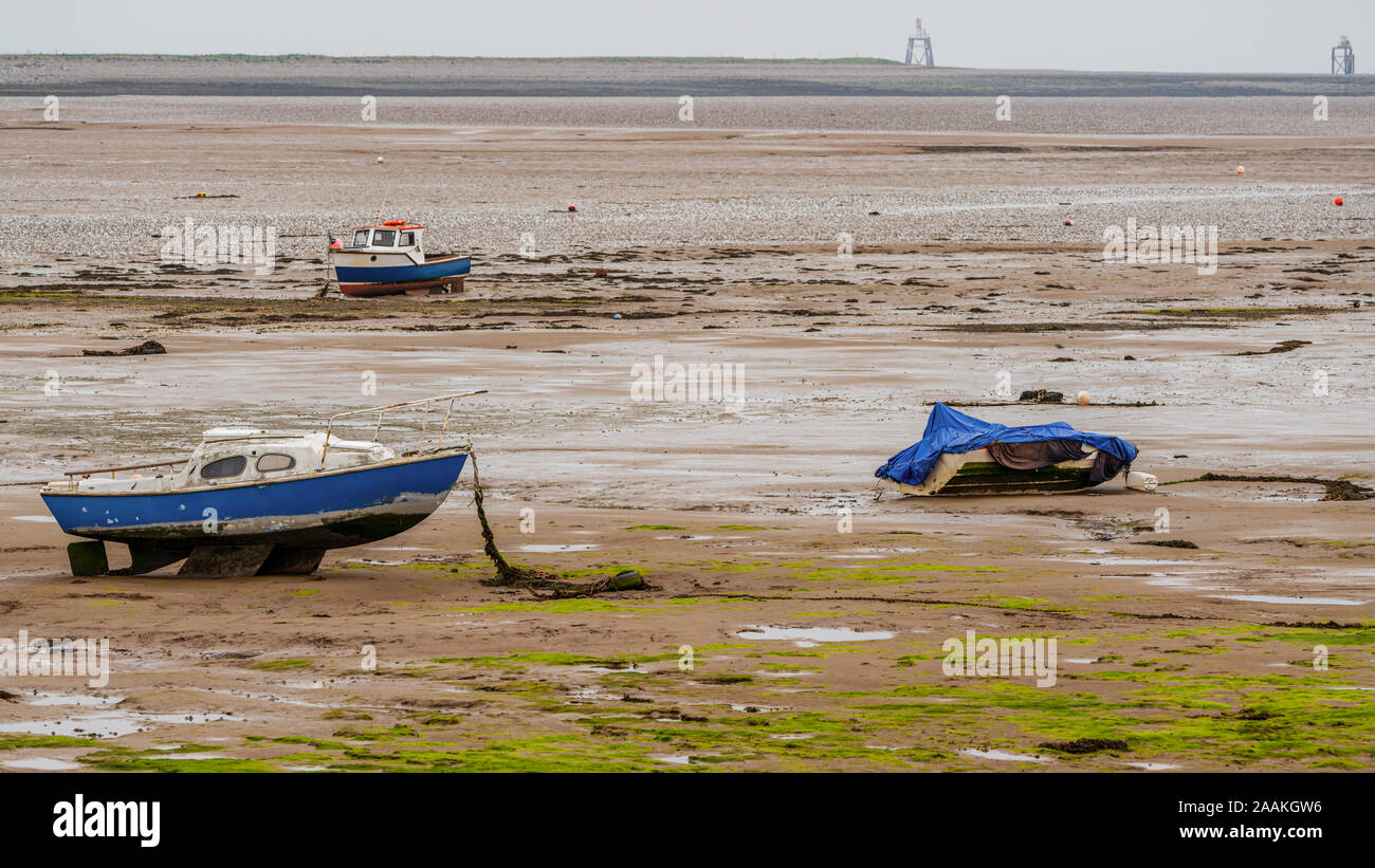 Three boats in the mud of the Walney Channel, seen from the road to Roa Island, Cumbria, England, UK Stock Photo