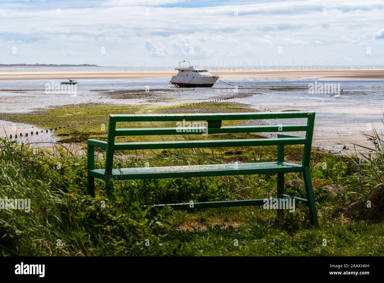 A bench with a view towards two boats in the low tide and the Ormonde