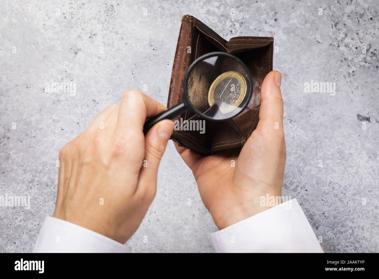 One euro in the wallet. A man is looking for money in a wallet with a magnifying glass. Small income concept Stock Photo