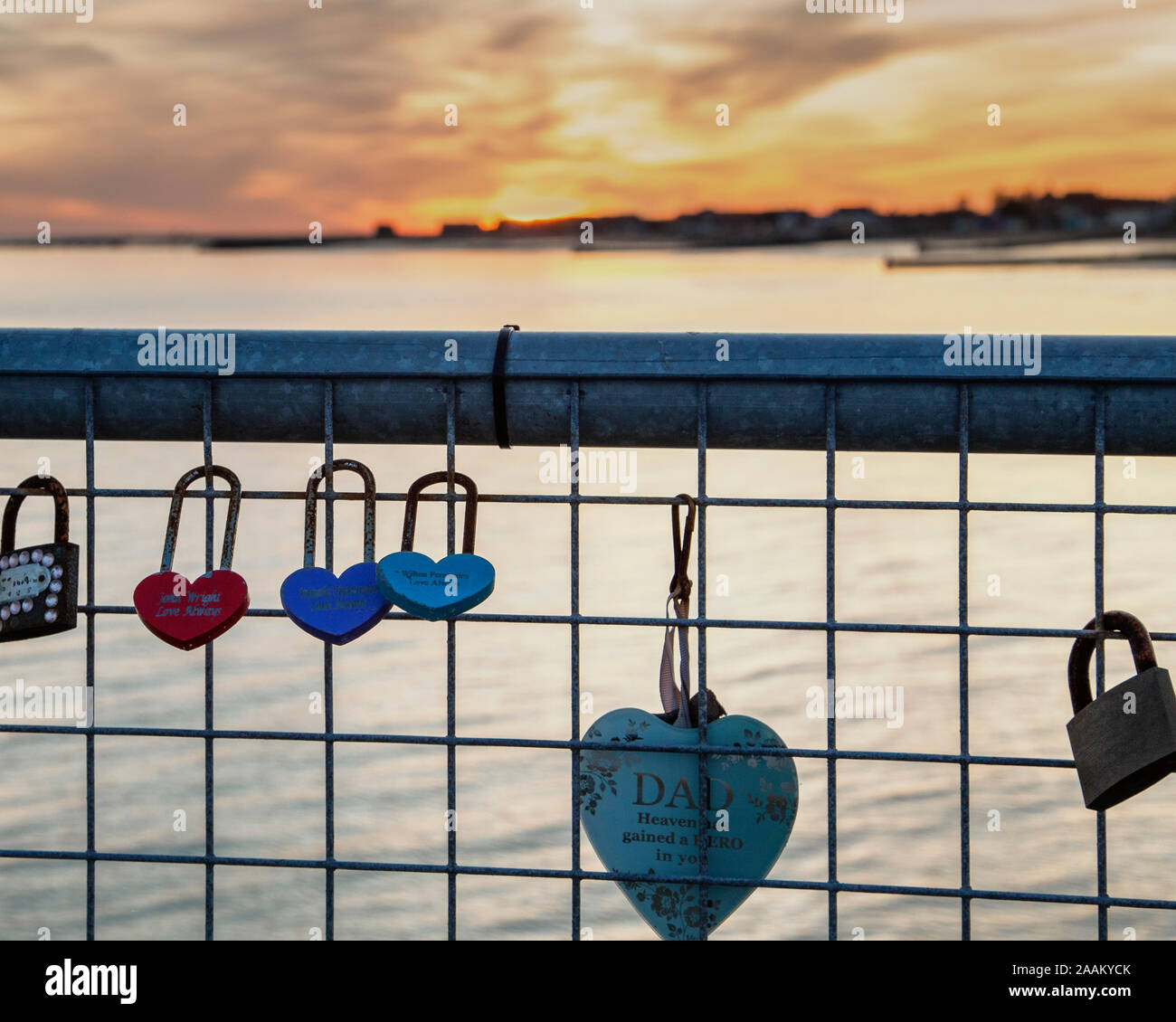 Love locks attached to a railing with a sunset in the distance. Concept of sun setting on a relationship, falling out of love and breaking up. Stock Photo