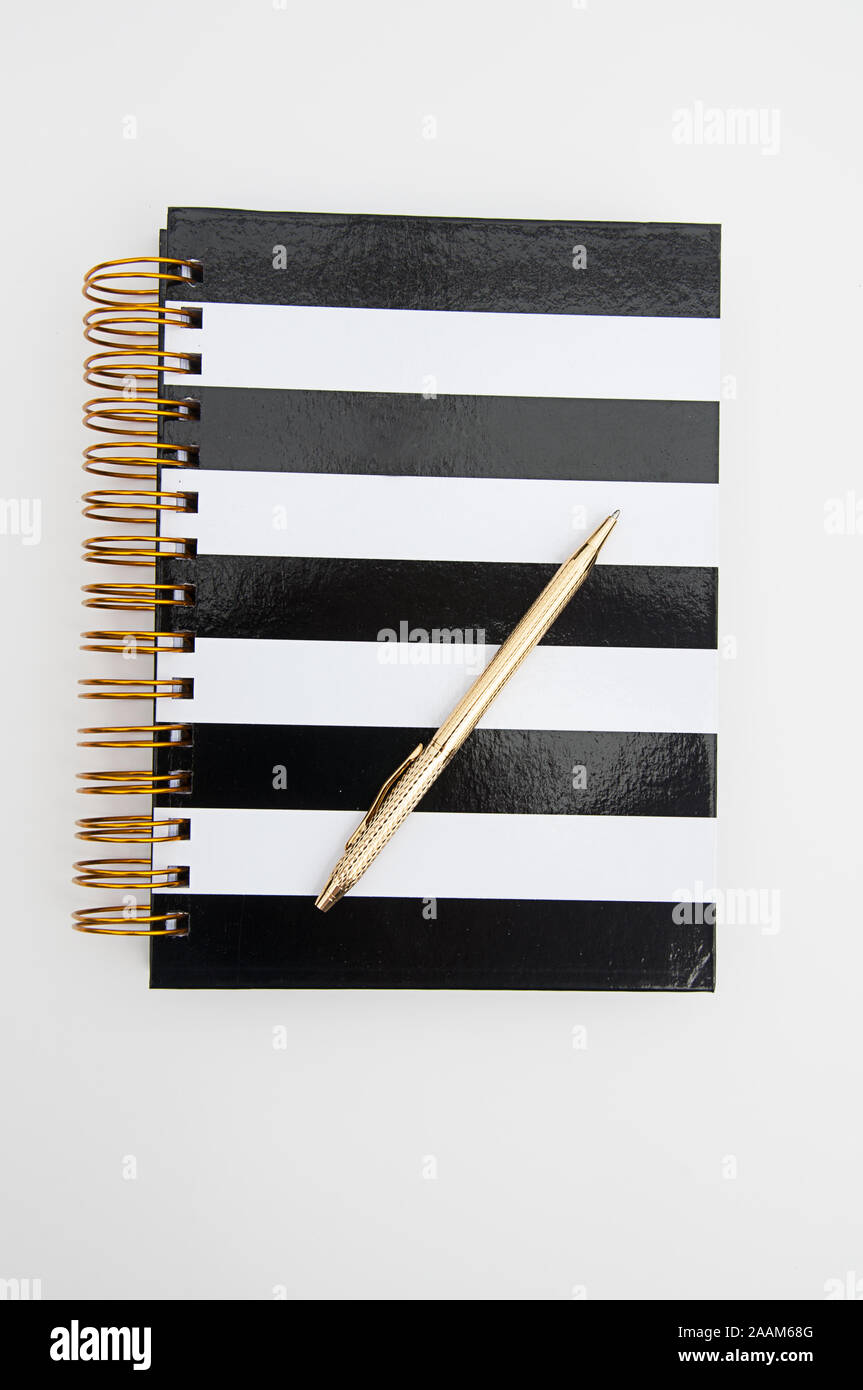 Diary striped black and white book with gold ring binders and a shiny gold pen writing instrument isolated on a light background.  Great for business Stock Photo