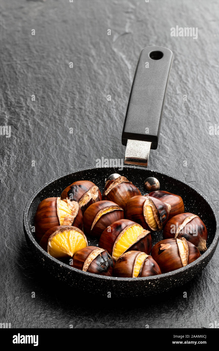 Premium Photo  Roasted chestnuts in a chestnut pan skillet with holes on a  aged brown wooden table