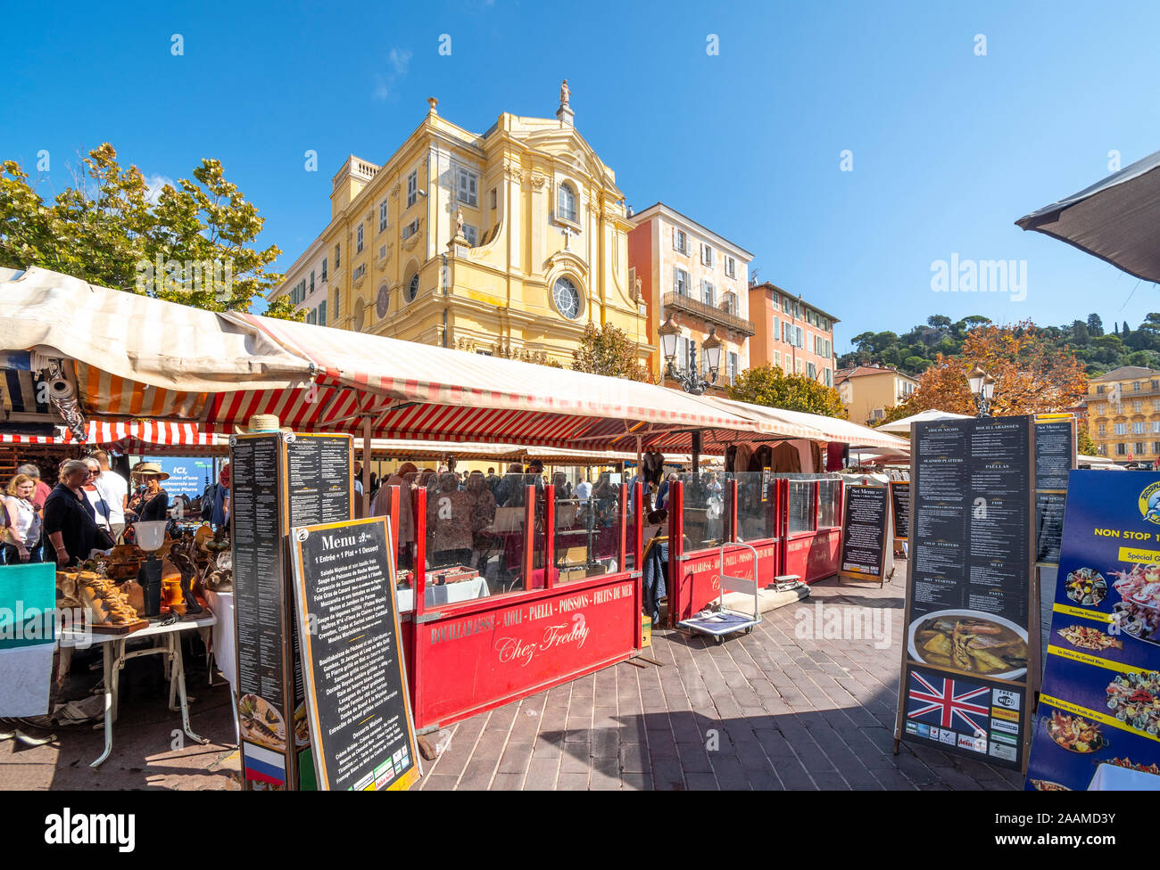 Tables with antiques and collectibles in the covered outdoor flea market alongside sidewalk cafes in the Cours Saleya market in Nice, France. Stock Photo