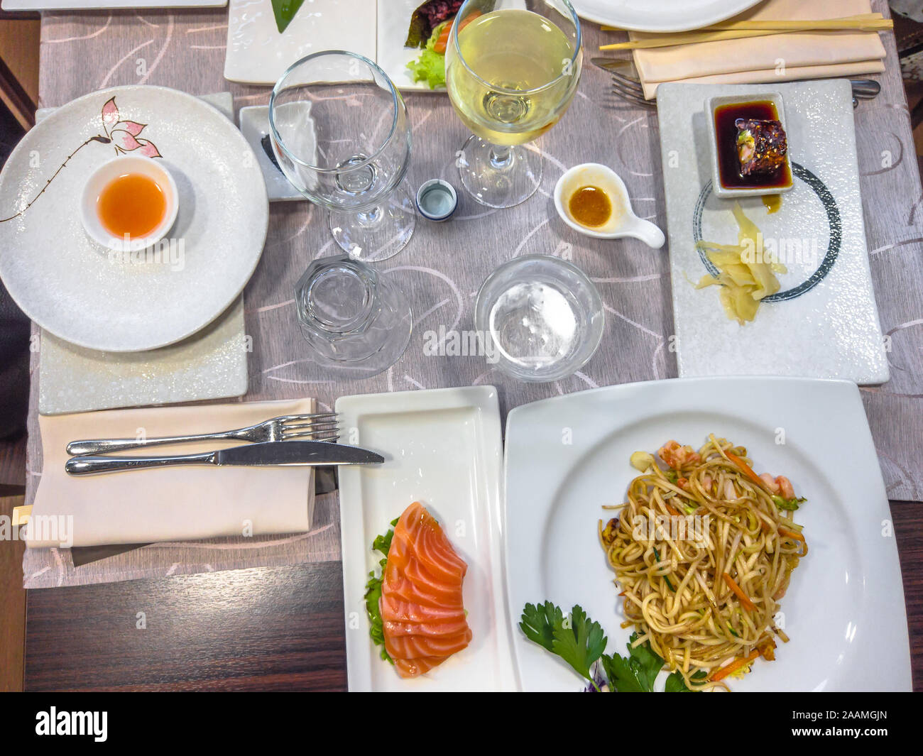 Japanese and Chinese fusion cuisine on a table full of delicious dishes. fresh salmon sushi, , shrimps spaghetti, surimi salad and white wine. Stock Photo