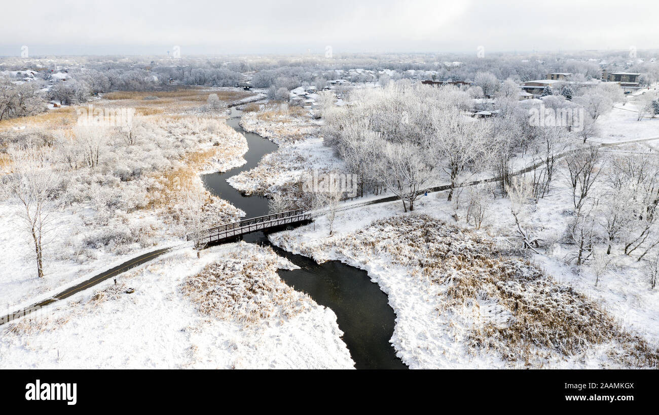 Drone / Aerial shot of a small bridge through a forest preserve and crossing over a river after a snow storm. Stock Photo
