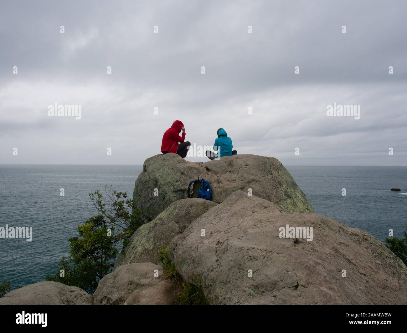 People Sitting On Rocks Taking In An Ocean View Stock Photo