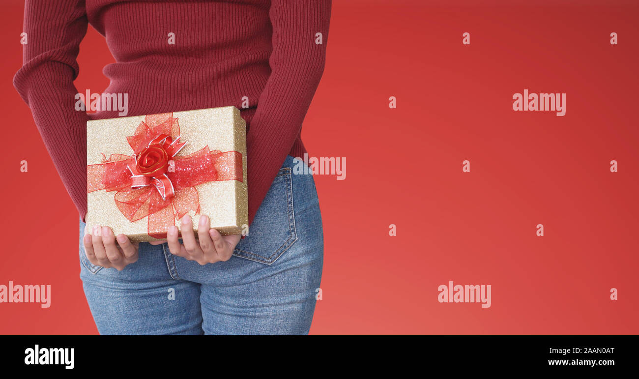 Woman holding gift box behind, on red background Stock Photo