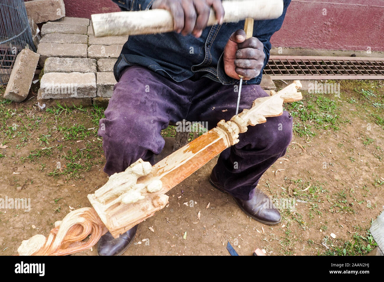 closeup of an African black man, skilled craftsman, artisan carving wood making traditional figurines and showing movement by his hands moving Stock Photo