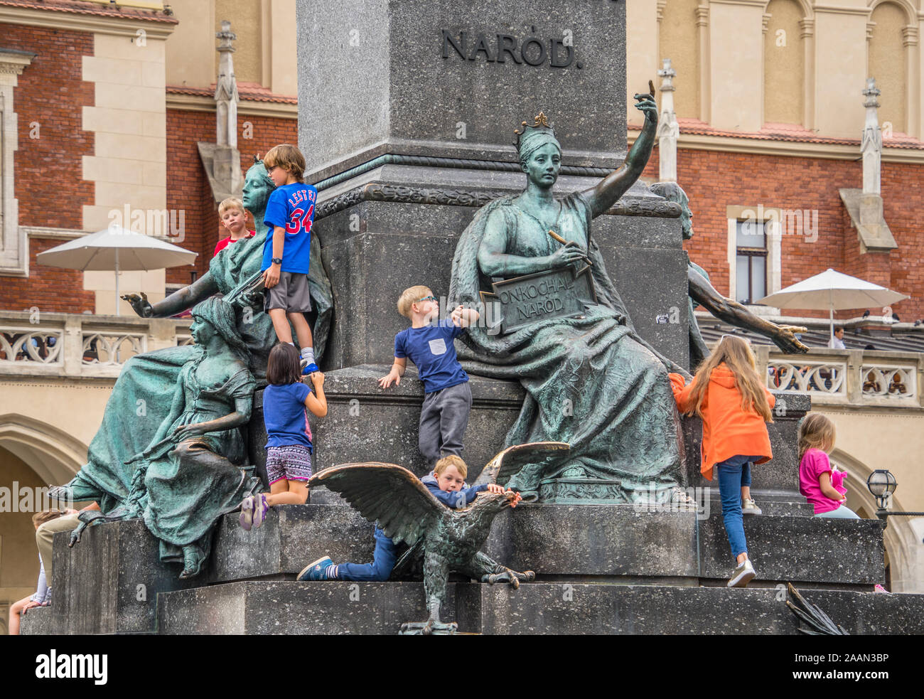 children frollicking amongst the allegoric figures at the base of the Adam Mickiewicz Monument on Krakow's main square next to the iconic Cloth Hall, Stock Photo