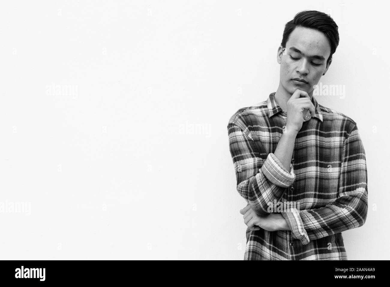 Young handsome Indian man against white wall outdoors in black and white Stock Photo