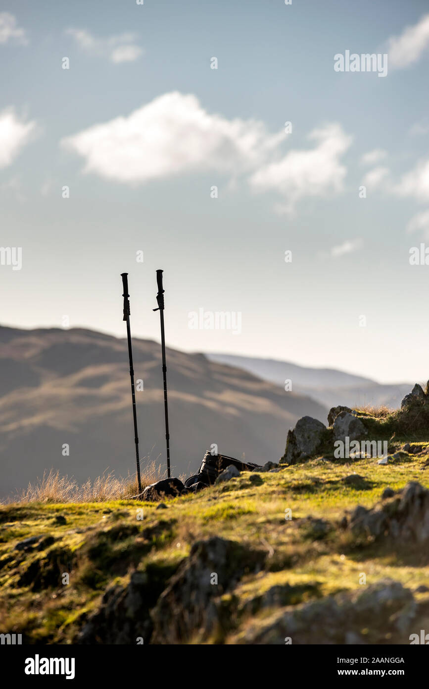 Walking poles and backpack on ground of hills in Lake District iwth mountains and bright Autumn Fall sky hiting landscape in background Stock Photo