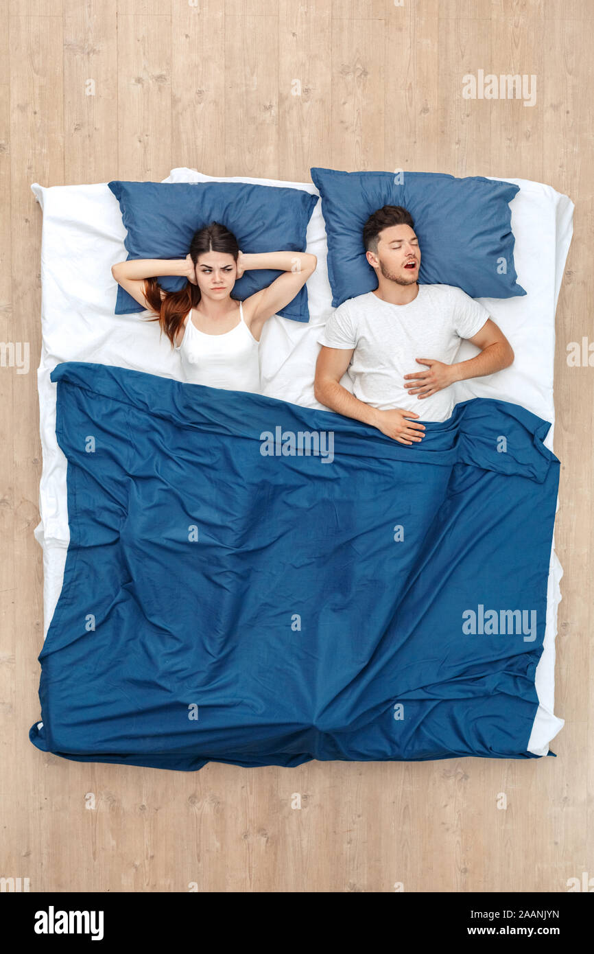 Bedtime. Young man sleeping yawning while woman covering ears concerned