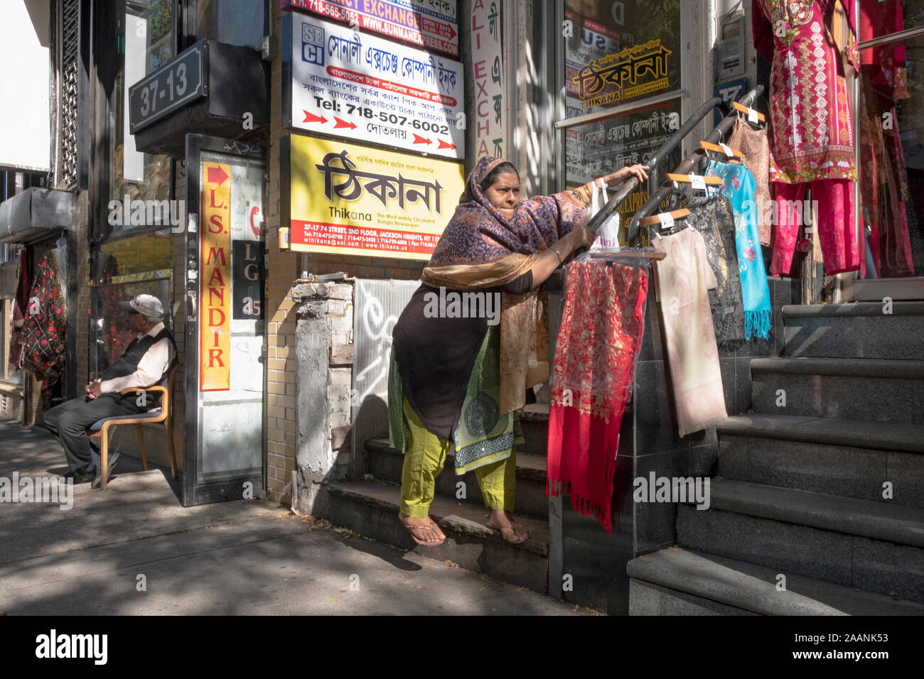 An older Islamic woman walks down ta set of stairs with difficulty using both hands for support. In Jackson Heights, Queens, New York City. Stock Photo