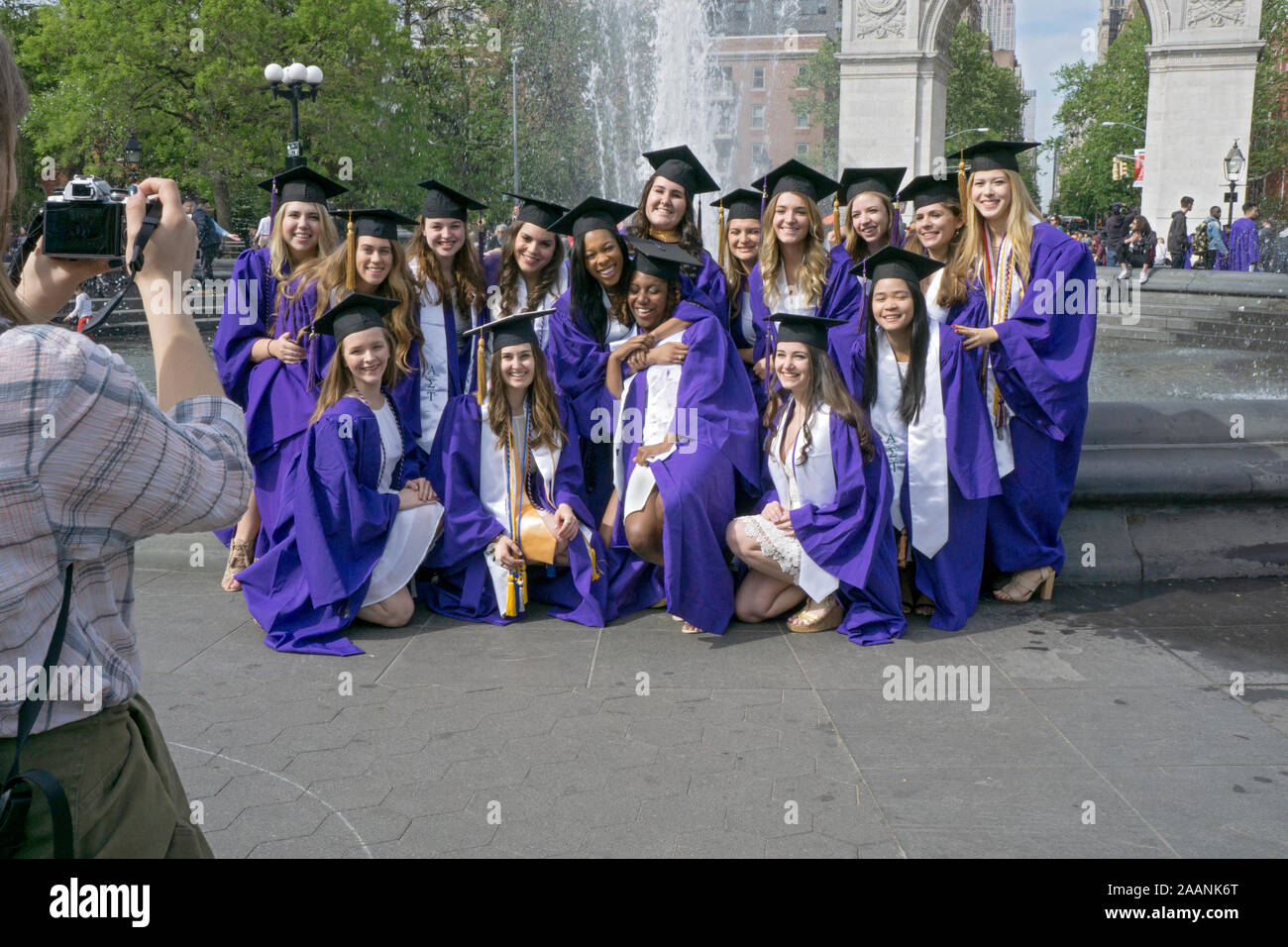 A diverse group of women pose for a photo in their graduation caps & gowns in front of the fountain in Washington Square Park in Greenwich Village, NY Stock Photo
