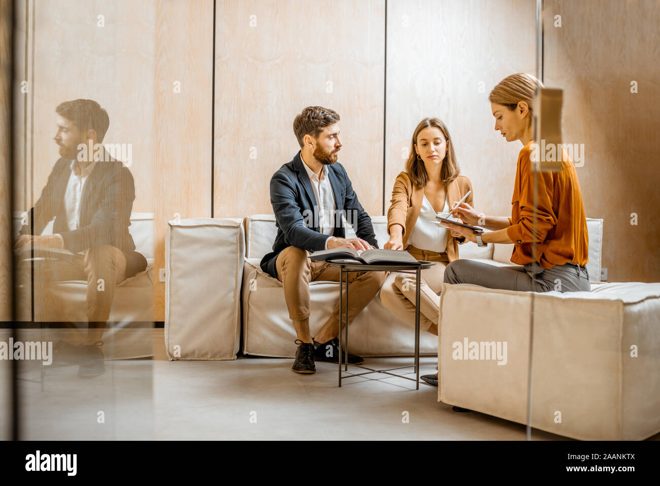 Young couple talking with a sales manager or real estate agent, sitting on the comfortable couch in the office Stock Photo