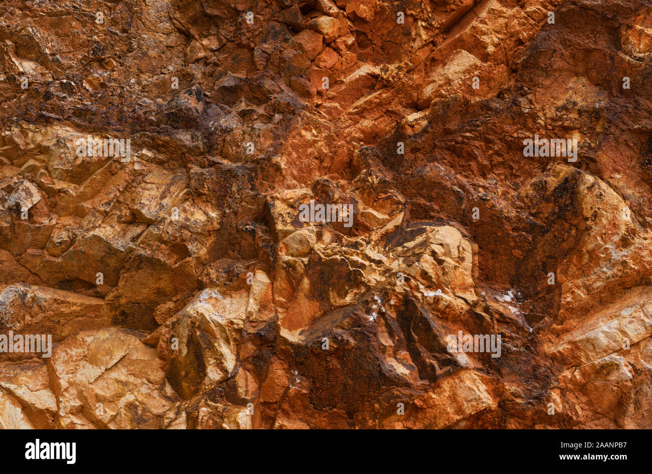Rocky wall in orange and gold tones of the old gold mines of Rodalquilar in the province of Almeria in Spain. Stock Photo