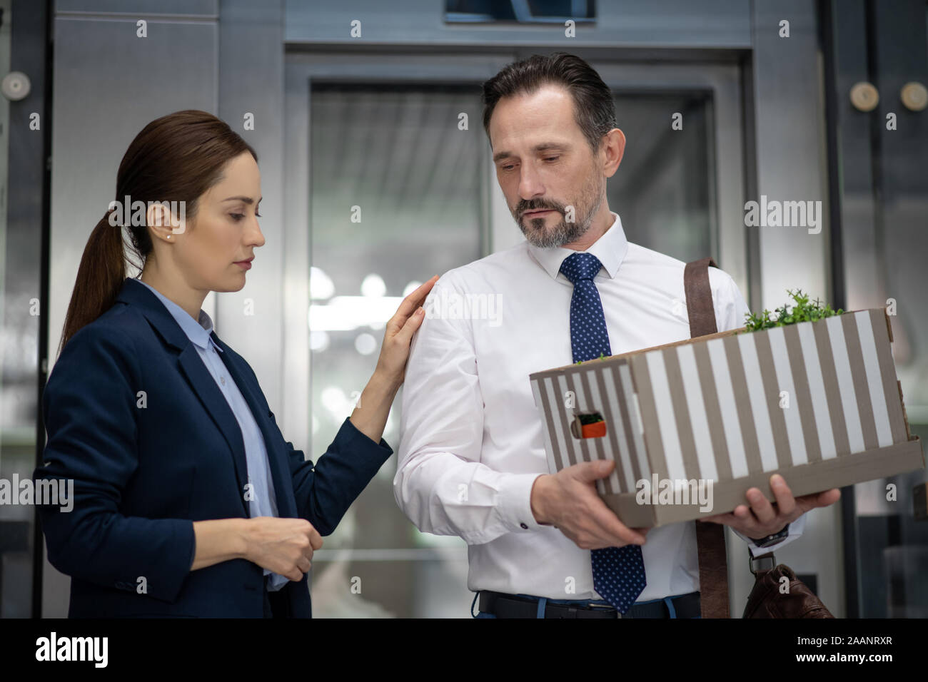 Dark-haired colleague supporting her friend from office after dismissal Stock Photo