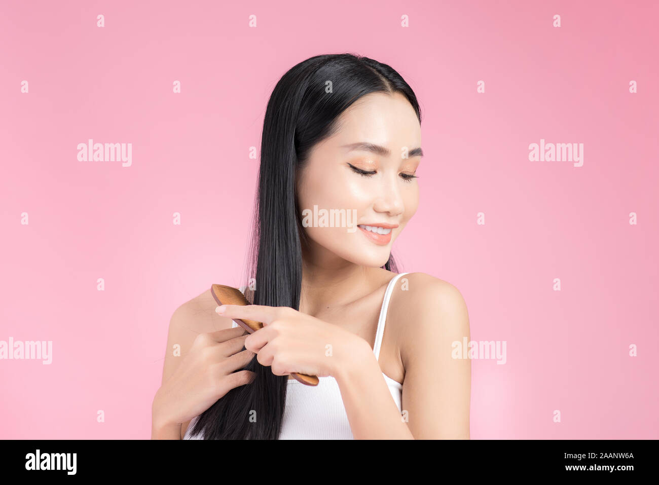 Beautiful young Asian woman holding her healthy hair and combing her hair on pink background. Stock Photo
