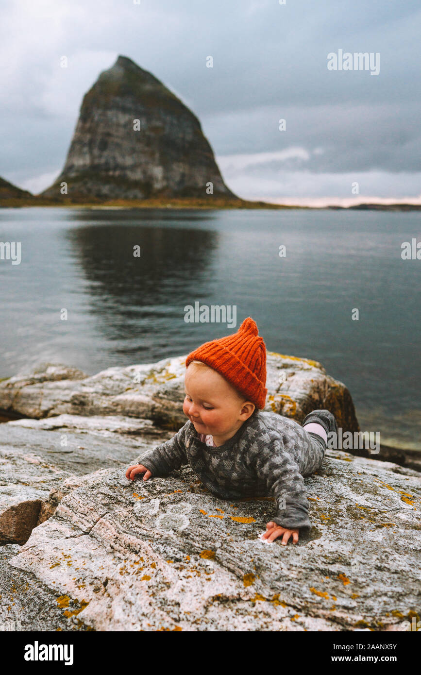 Baby travel in Norway crawling on scandinavian beach with island rocks view family adventure lifestyle vacations activity outdoor cute child with oran Stock Photo
