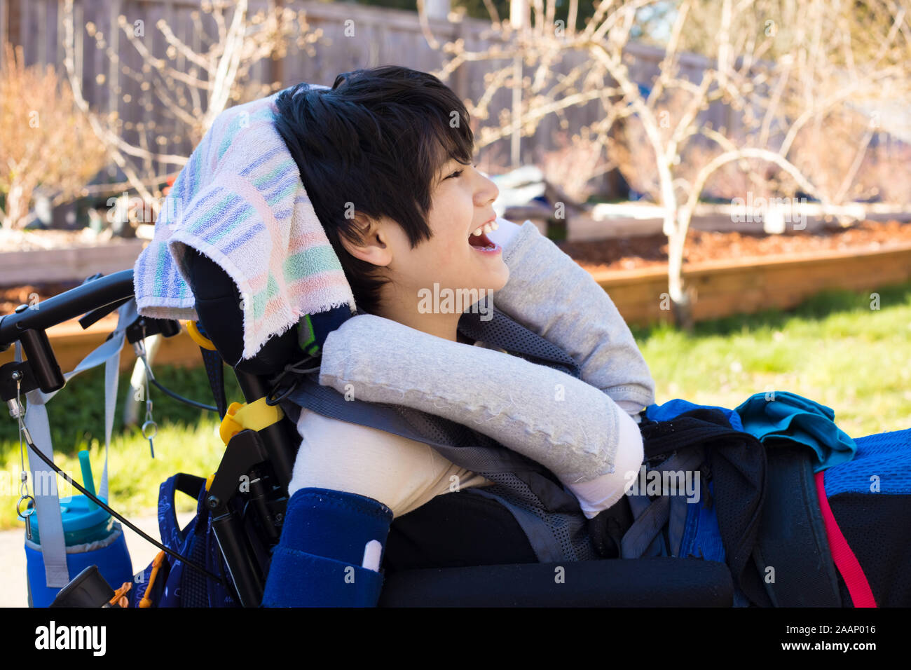 Handsome eleven year old disabled biracial boy in wheelchair sitting outdoors on a summer day, smiling Stock Photo