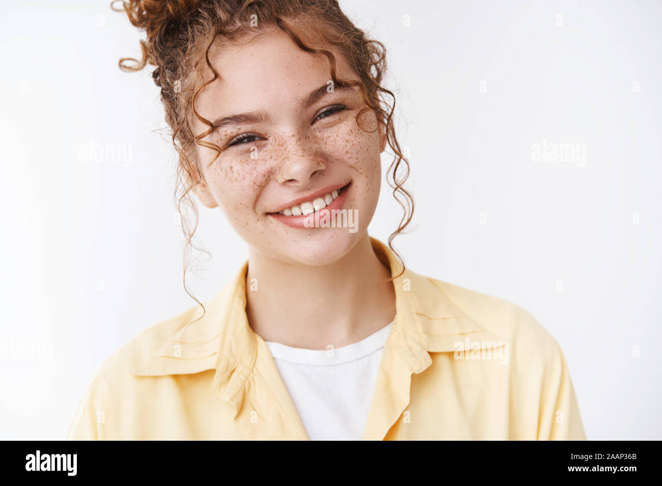 Gorgeous caucasian ginger girl freckles messy curly bun tilting head friendly pleasantly smiling expressing optimism, feel happy relaxed, standing Stock Photo