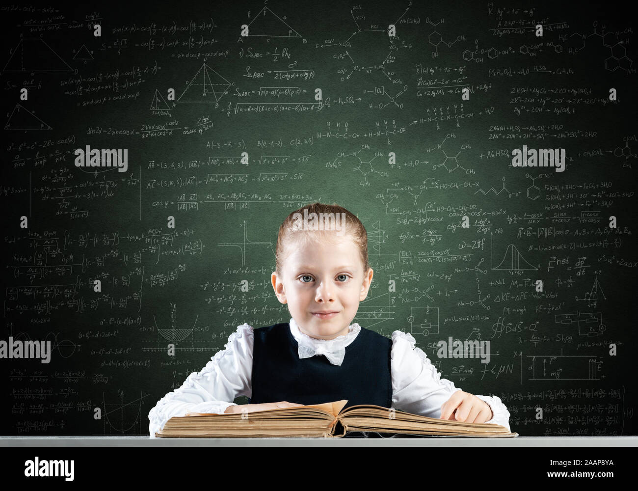 Smiling little girl sitting at desk with open book Stock Photo - Alamy