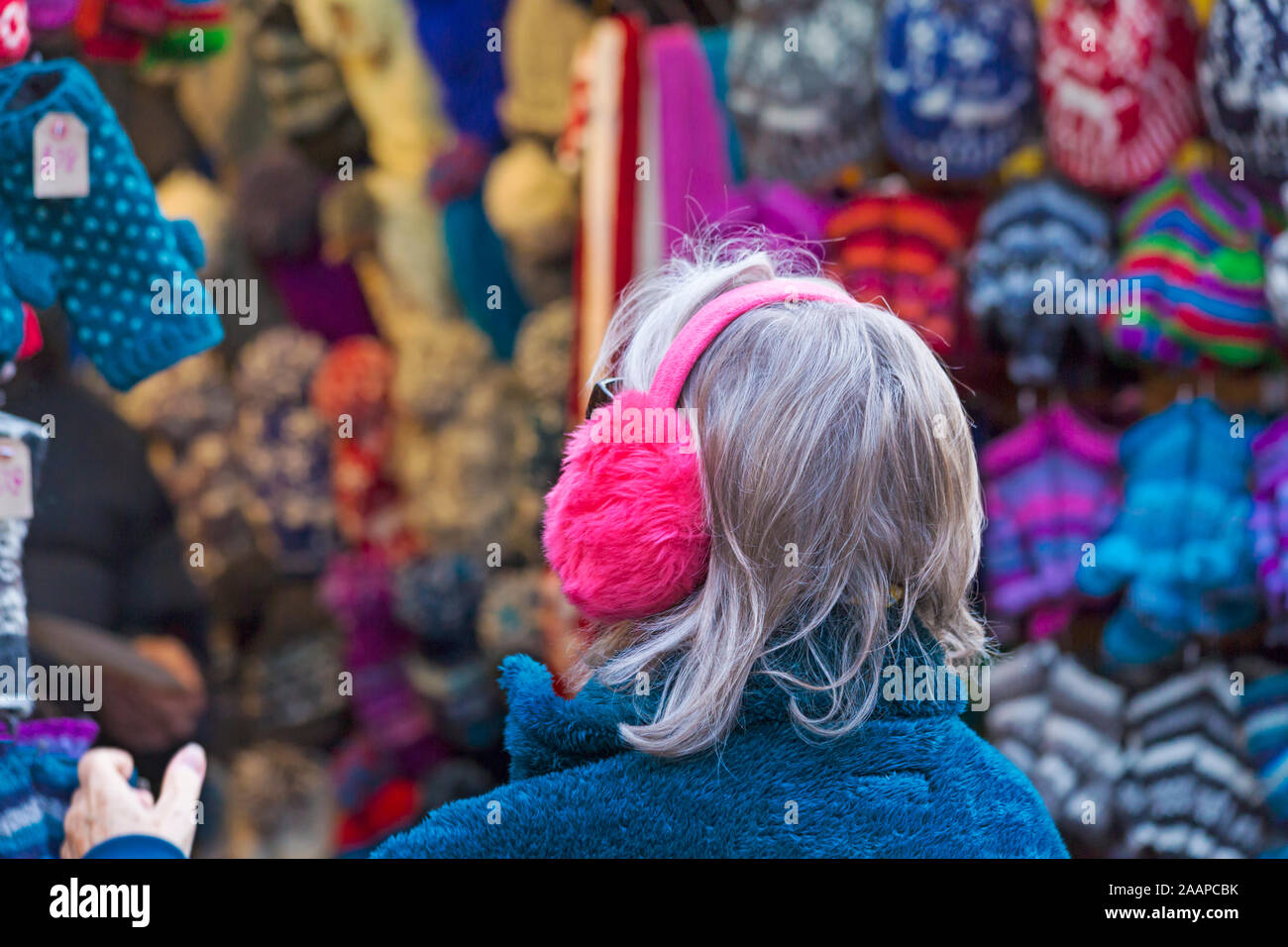 Woman wearing ear muffs looking at hats on market stall at Winchester Christmas Market, Winchester, Hampshire, UK in December Stock Photo