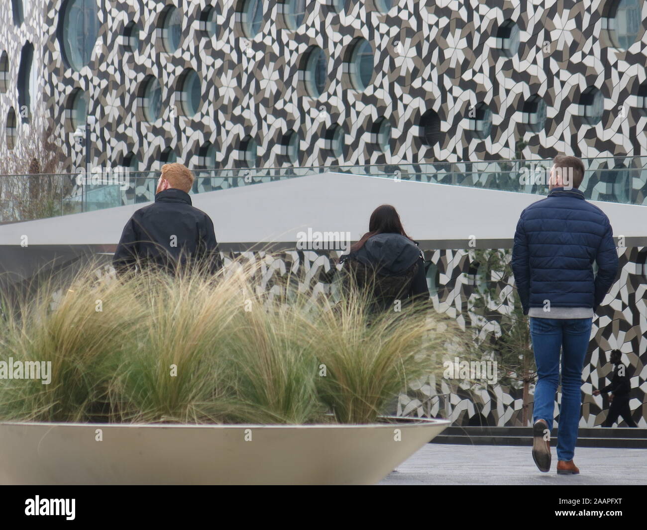 Three young people walk towards an eye-catching building, which has patterned mosaic cladding on the walls and round windows. Stock Photo