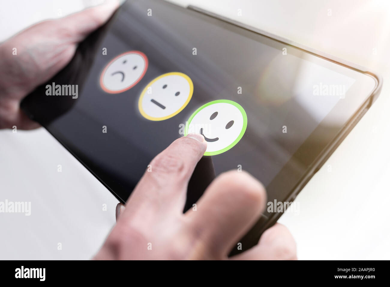 pleased person giving positive feedback by touching smiley face on digital tablet touchscreen, service quality rating concept. Stock Photo
