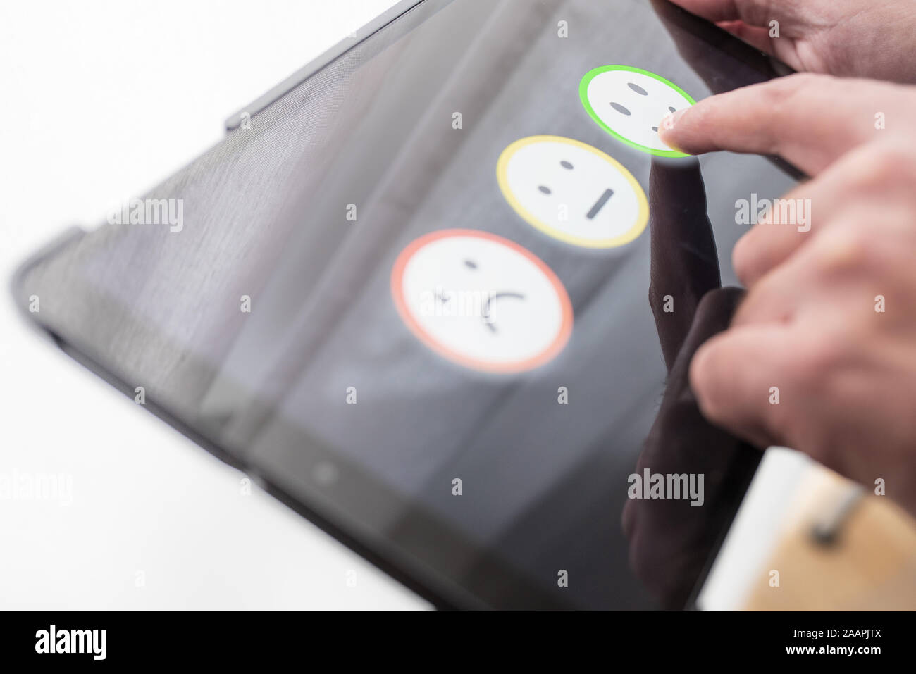 pleased person giving positive feedback by touching smiley face on digital tablet touchscreen, service quality rating concept.. Stock Photo