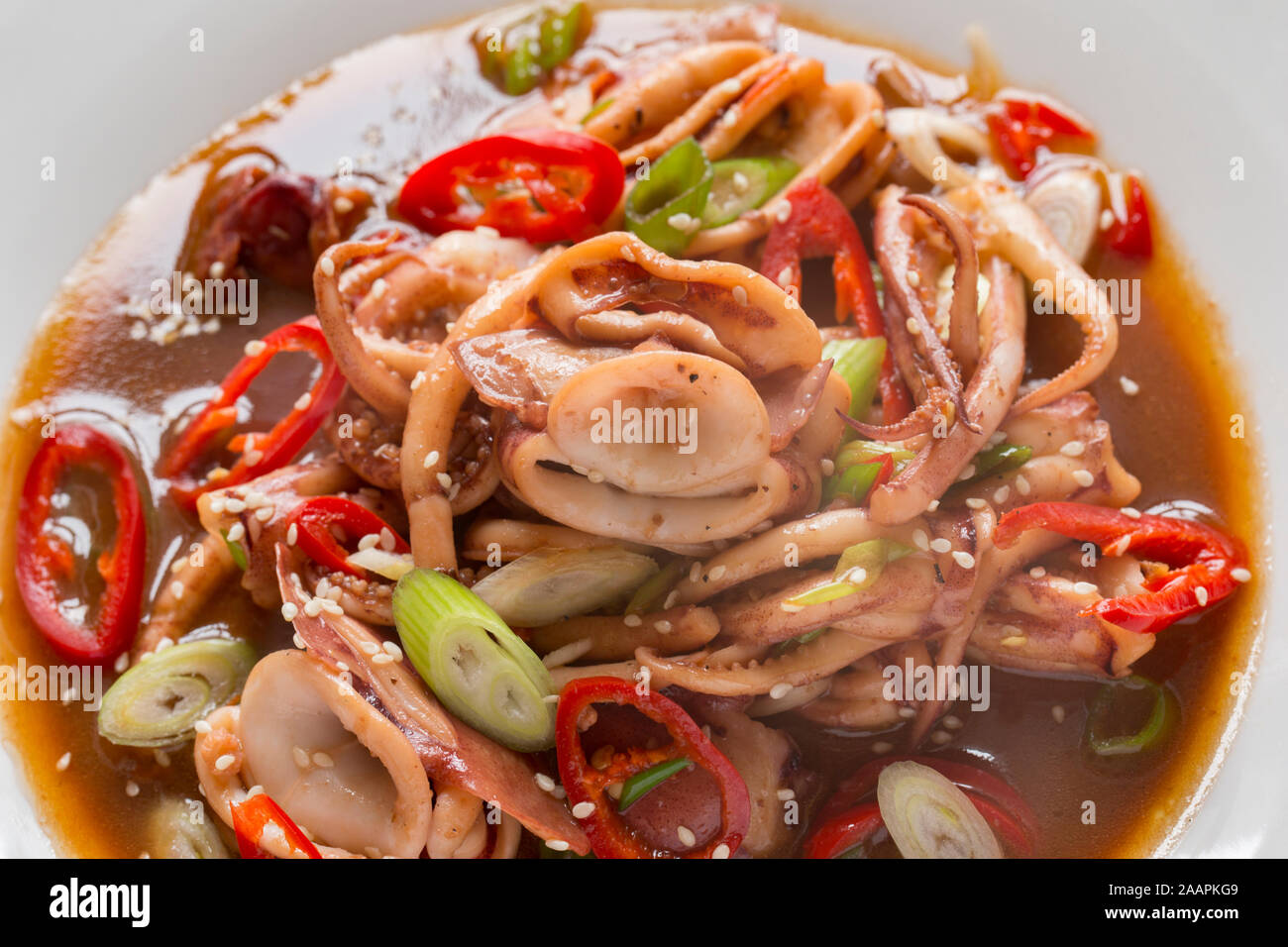 Fresh squid, caught in the English Channel, that has been fried in butter and oil with Teriyaki sauce, Szechuan pepper, spring onions and red chillis Stock Photo