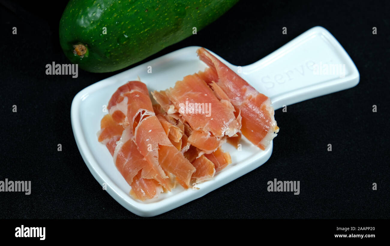 Sliced jamon on white dish with avocado decoration Stock Photo