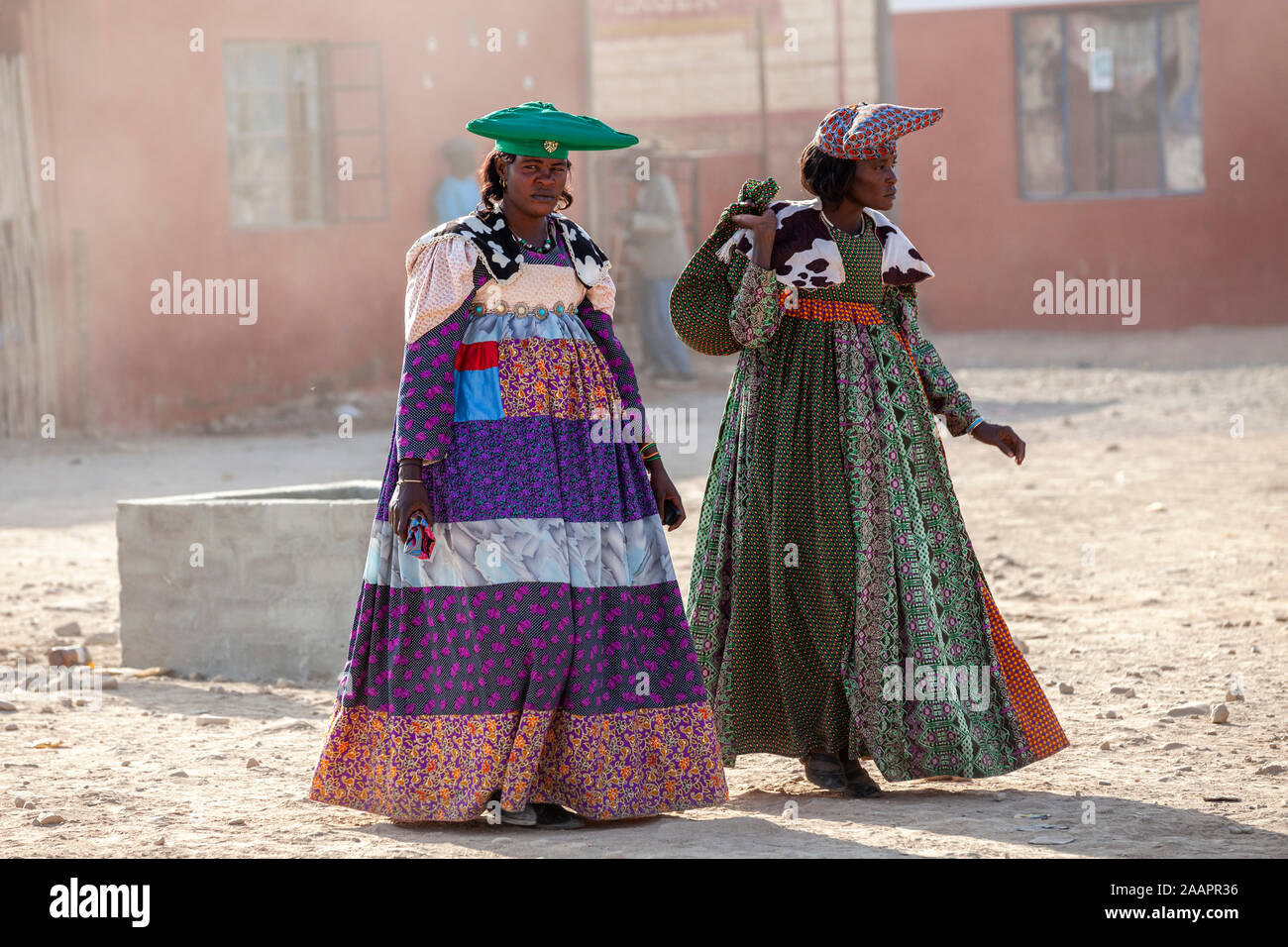 Herero women in traditional dress and horned hat walk at a street of Opuwo town in Namibia, Africa Stock Photo