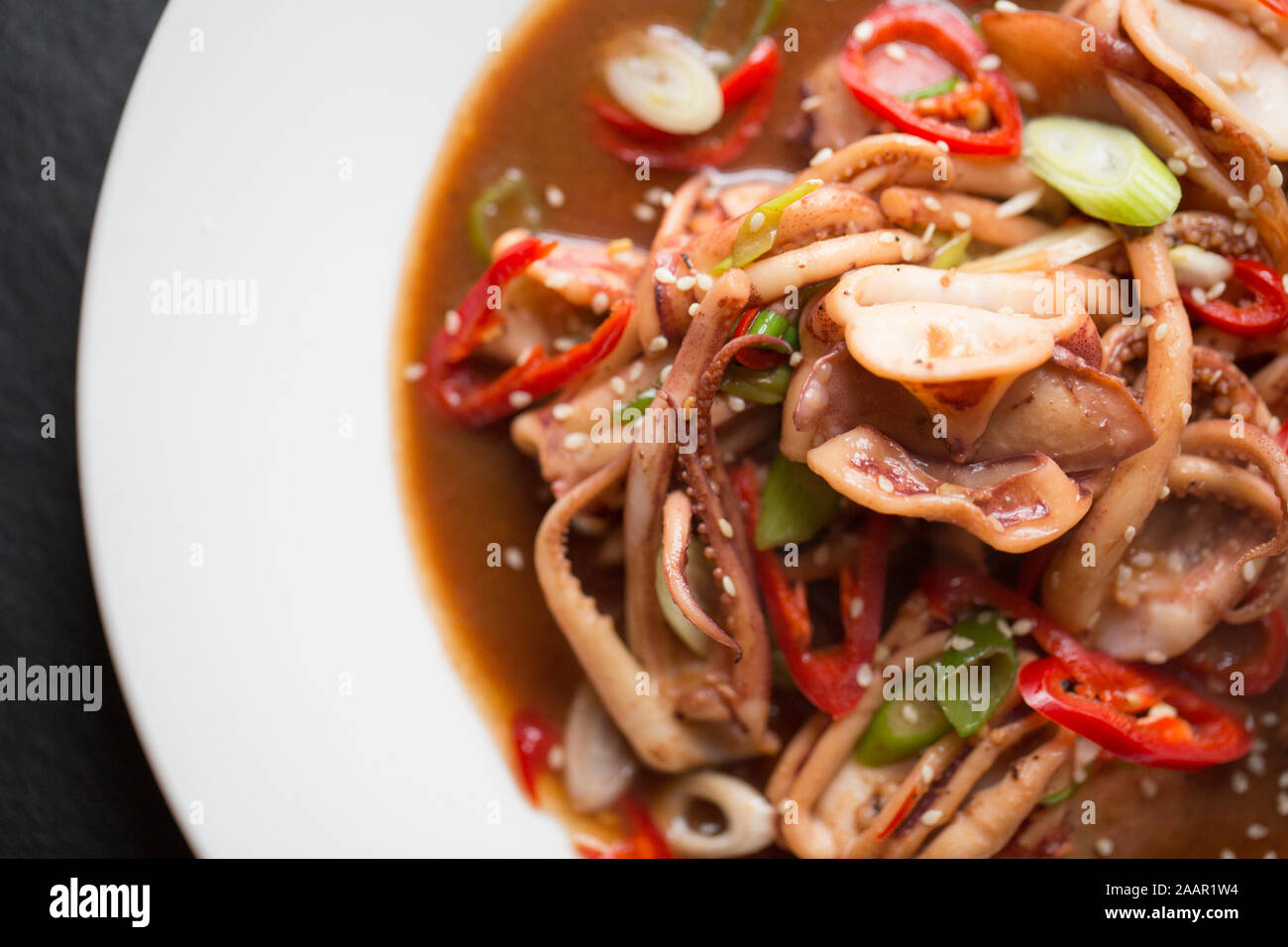 Fresh squid, caught in the English Channel, that has been fried in butter and oil with Teriyaki sauce, Szechuan pepper, spring onions and red chillis Stock Photo