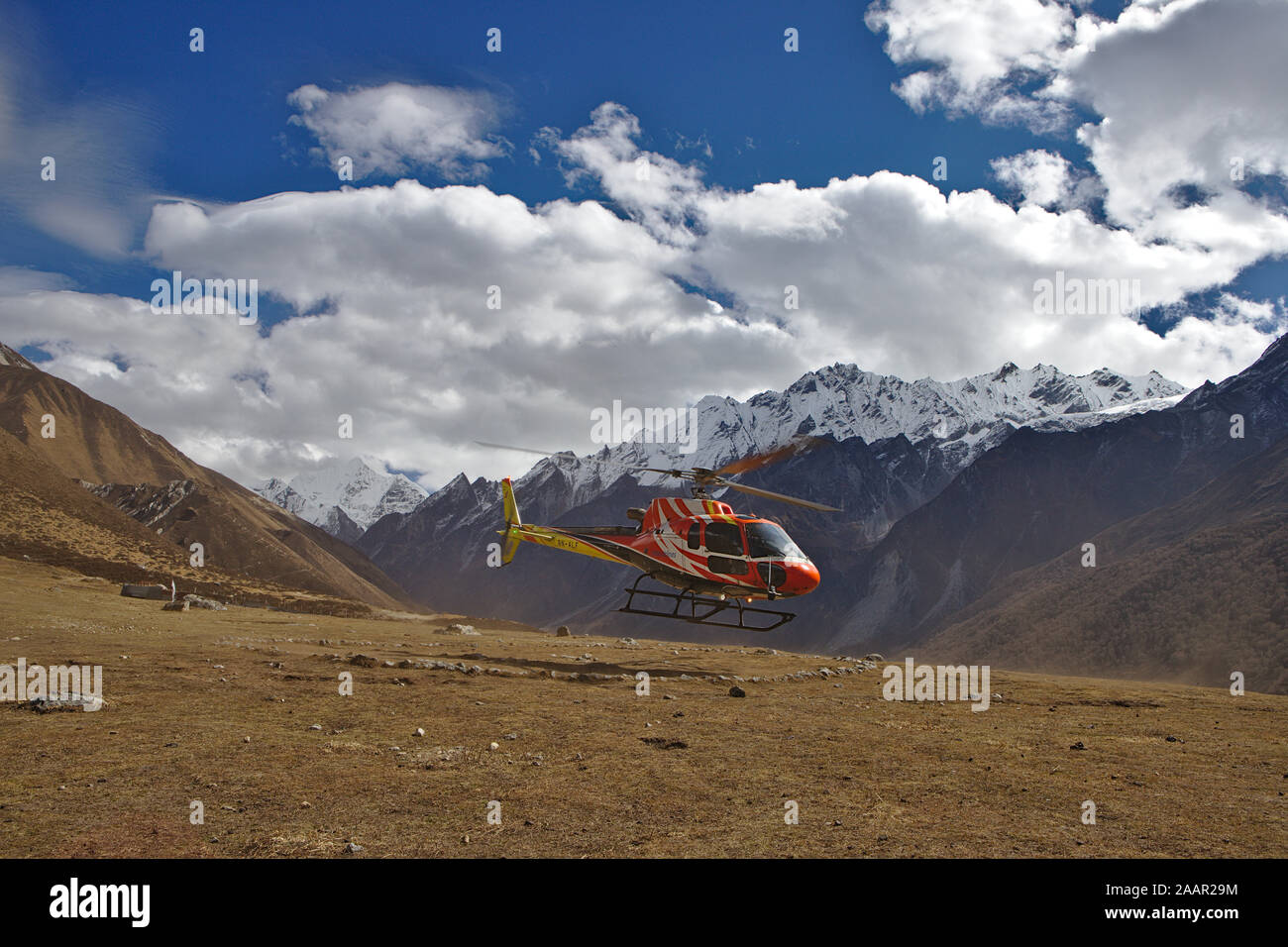 red and yellow helicopter coming in to land in Kyanjin Gompa Stock Photo