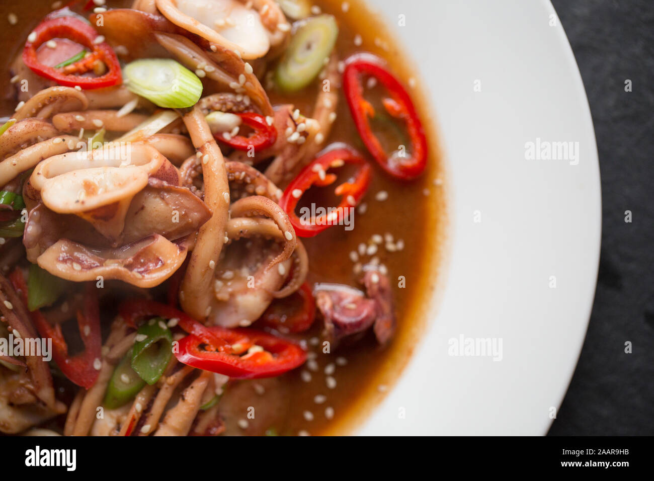 Fresh squid, caught in the English Channel, that has been fried in butter and oil with Teriyaki sauce, Szechuan pepper, spring onions and red chillis Stock Photo