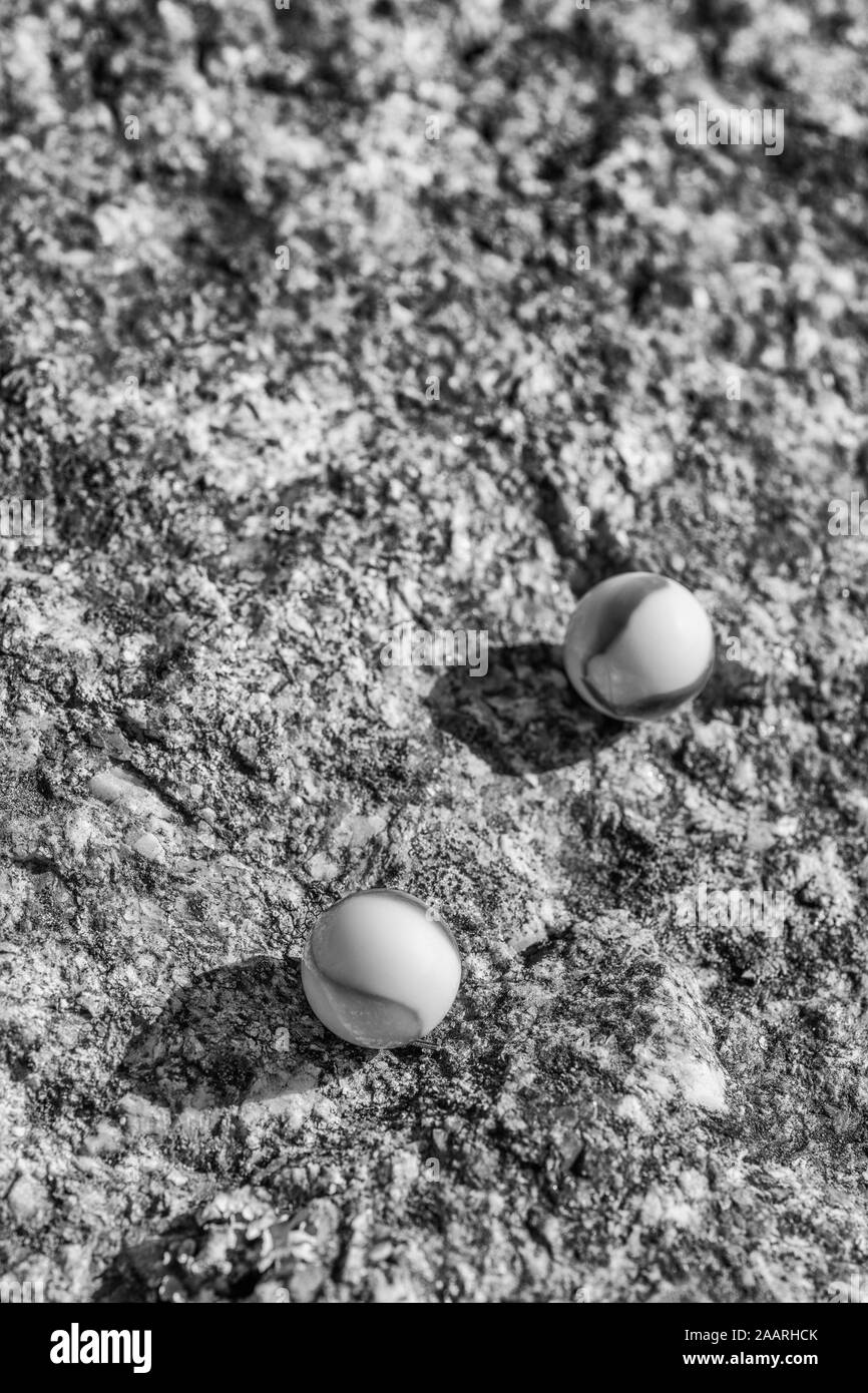 Black & white glass marbles on rough stone surface. For something lost, mental health, losing your marbles, abstract spheres, dreams, Biden & marbles. Stock Photo