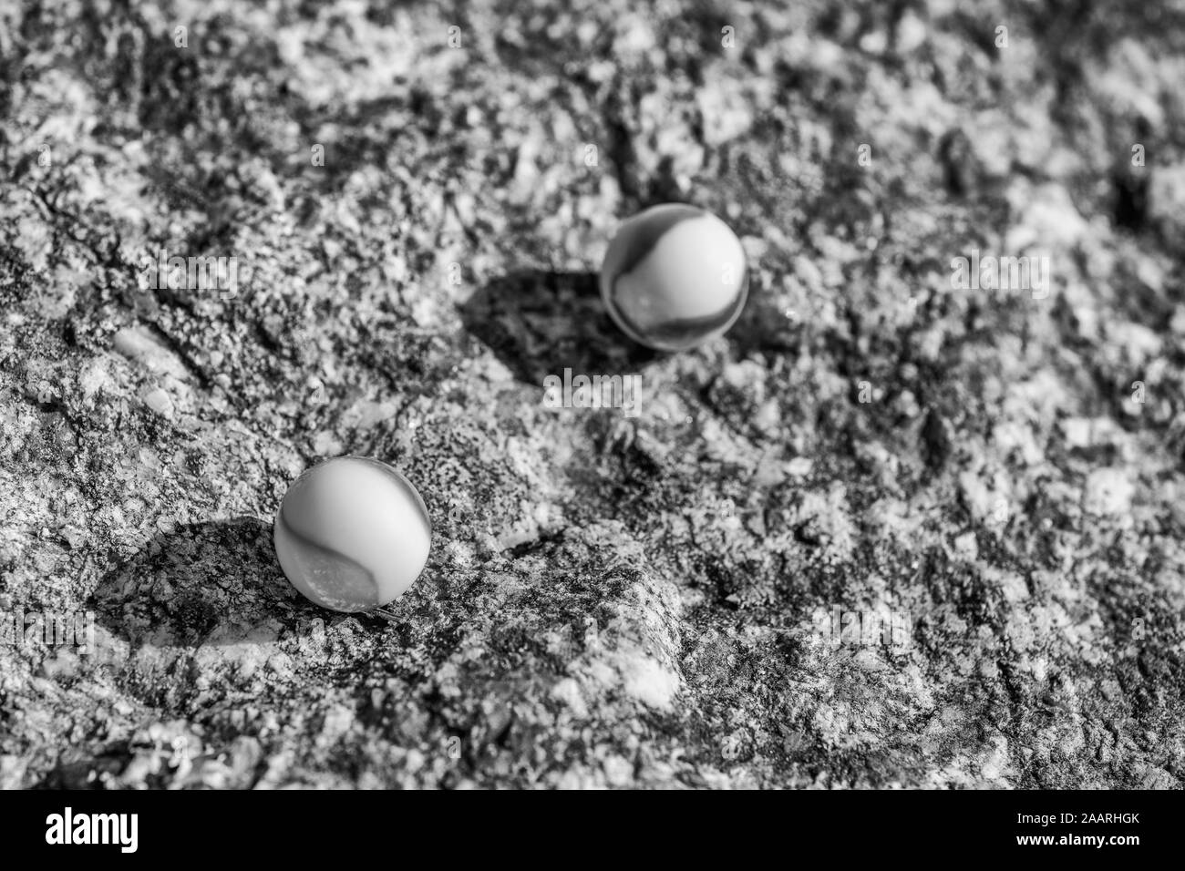 Black & white glass marbles on rough stone surface. For something lost, mental health, losing your marbles, abstract spheres, dreams, Biden & marbles. Stock Photo