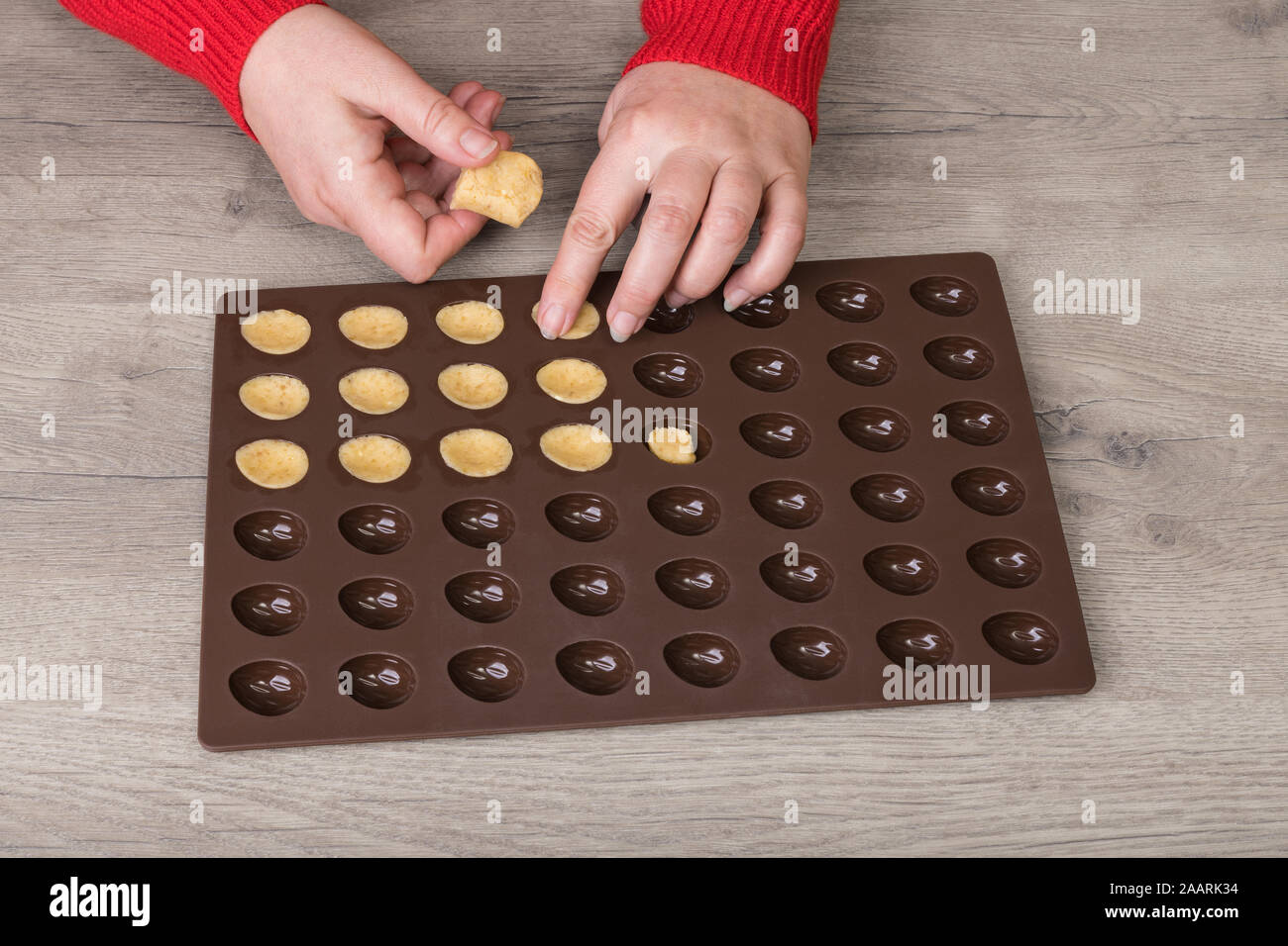 https://c8.alamy.com/comp/2AARK34/filling-raw-shortcrust-biscuit-dough-into-silicone-baking-mold-on-a-wood-background-female-hands-detail-and-traditional-christmas-sweets-in-nut-shape-2AARK34.jpg