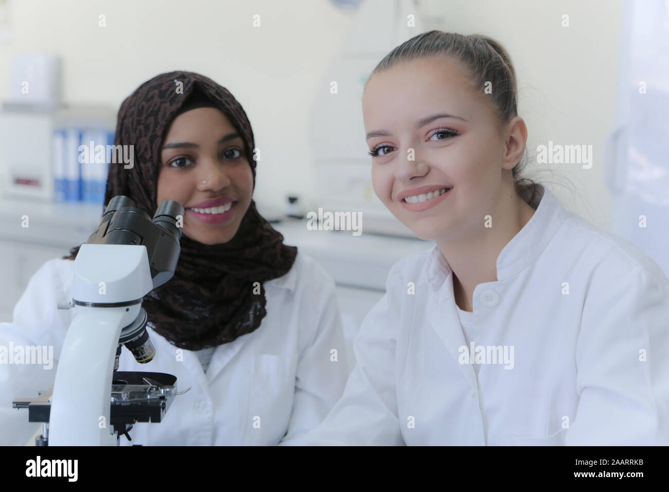 Two young female multiethnic scientists looking at camera and smilling ...