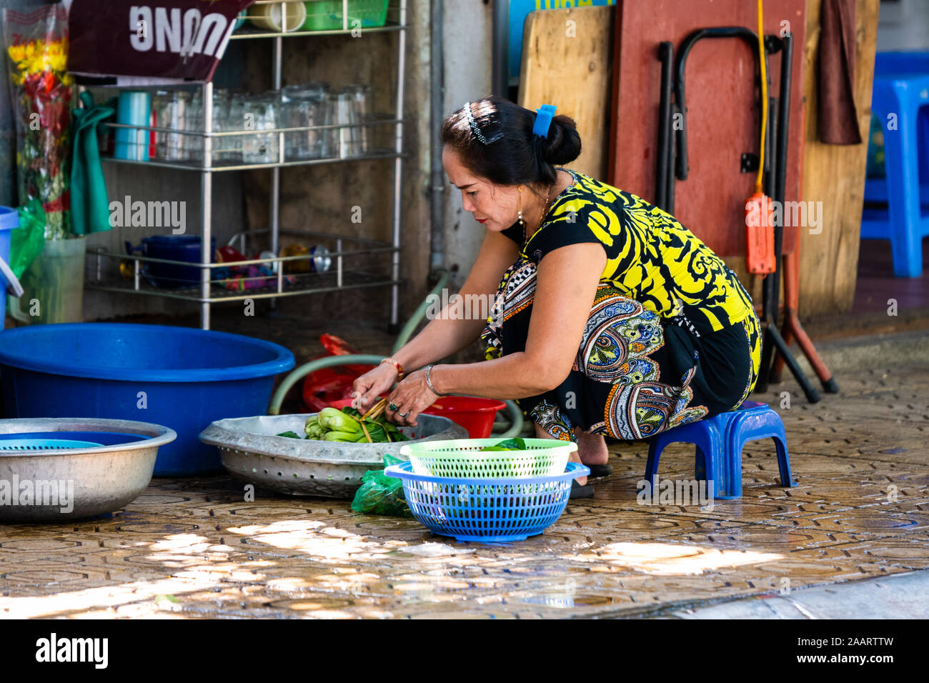 Hanoi, Vietnam - 12th October 2019: An Asian woman washes and prepares vegetables to sell as street food for lunch in the streets Stock Photo