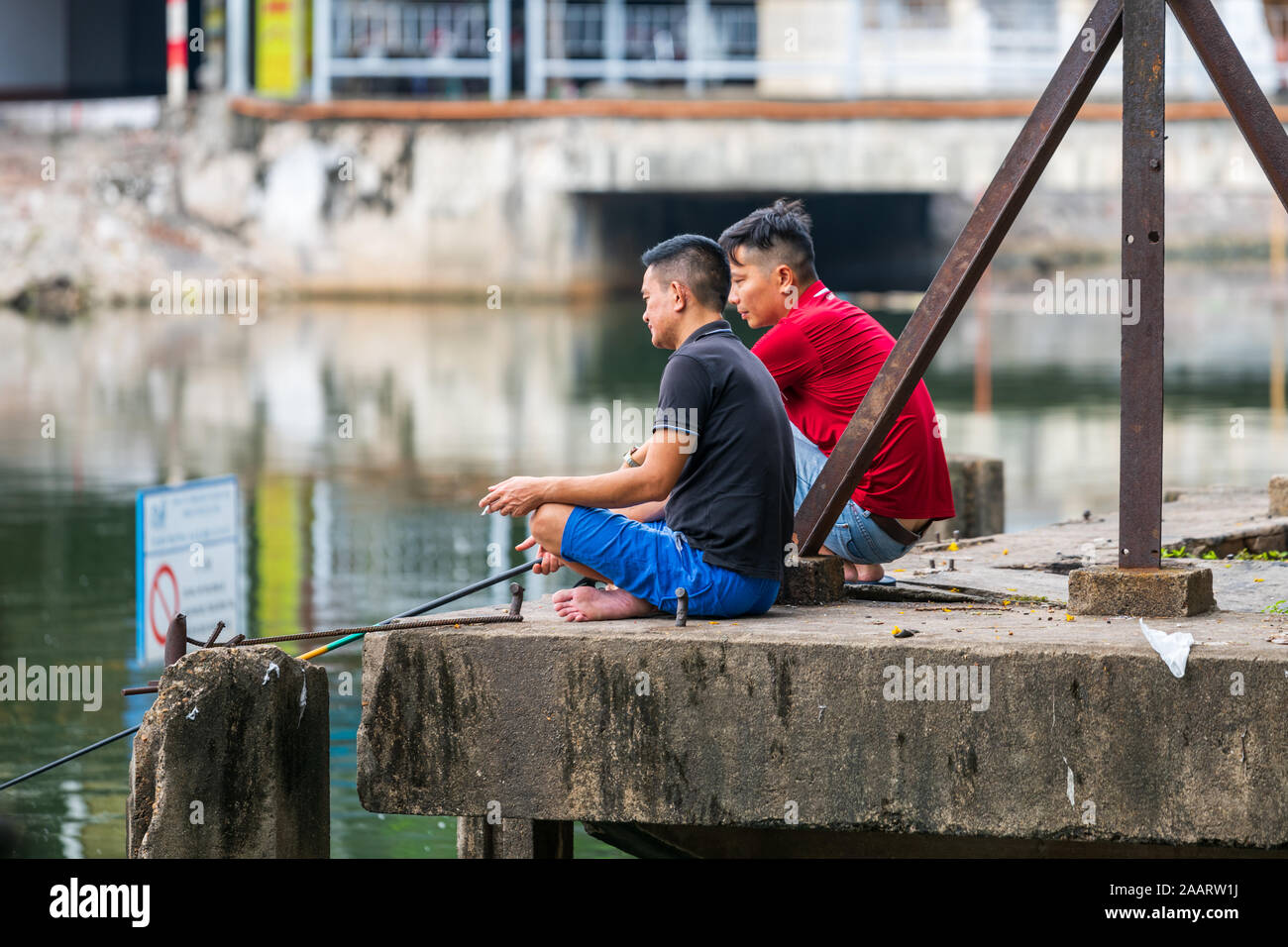 Hanoi, Vietnam - 12th October 2019: Two Asian men sit at the edge of a lake in Hanoi fishing for fish to cook for dinner Stock Photo