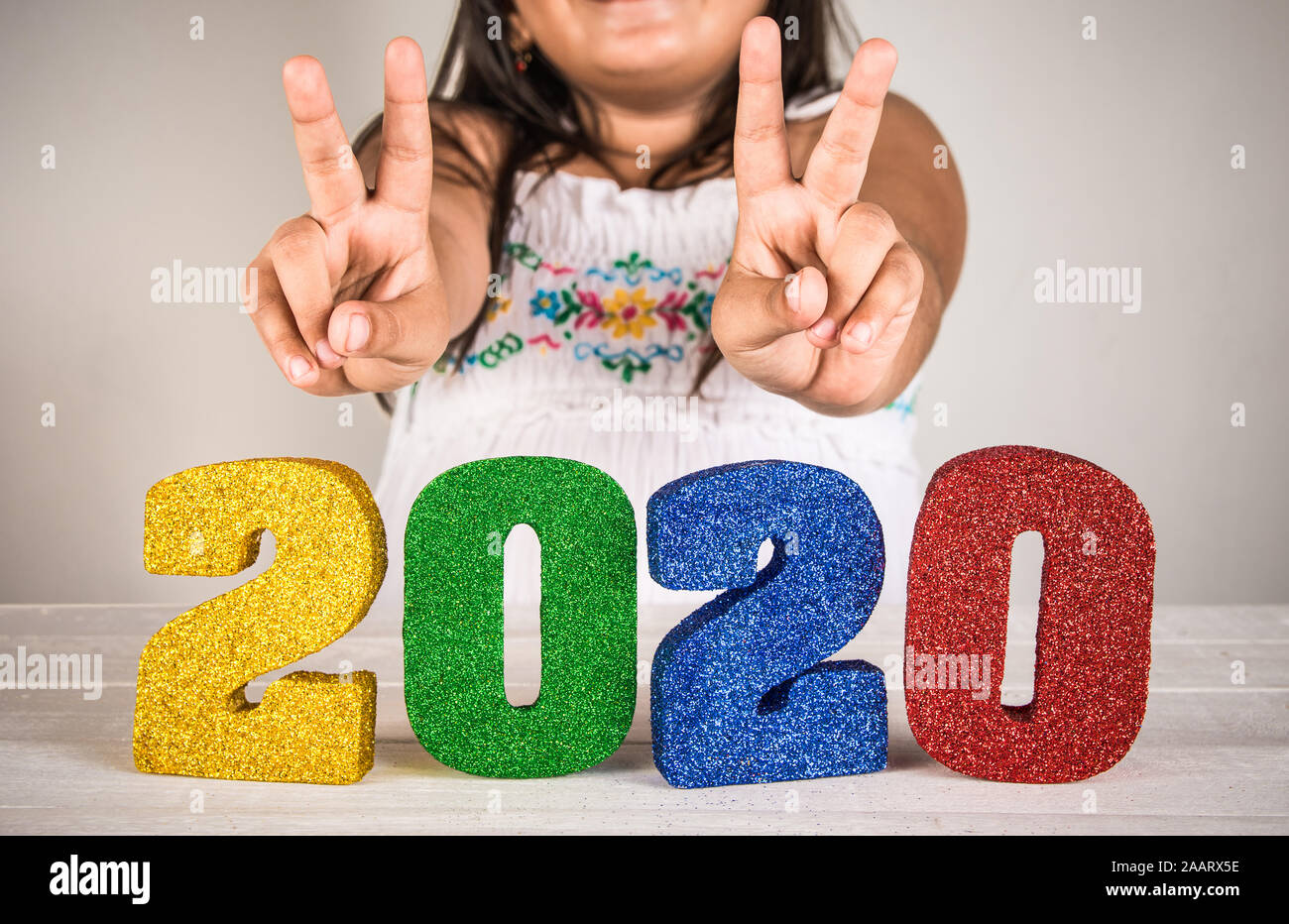 Young girl making peace sign above bright and colorful 2020 3d numbers - new years celebrations concept image. Stock Photo