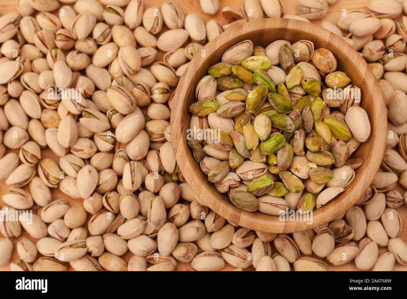 Top view of shell and peeled pistachios in wooden bowl and on wooden table. Stock Photo