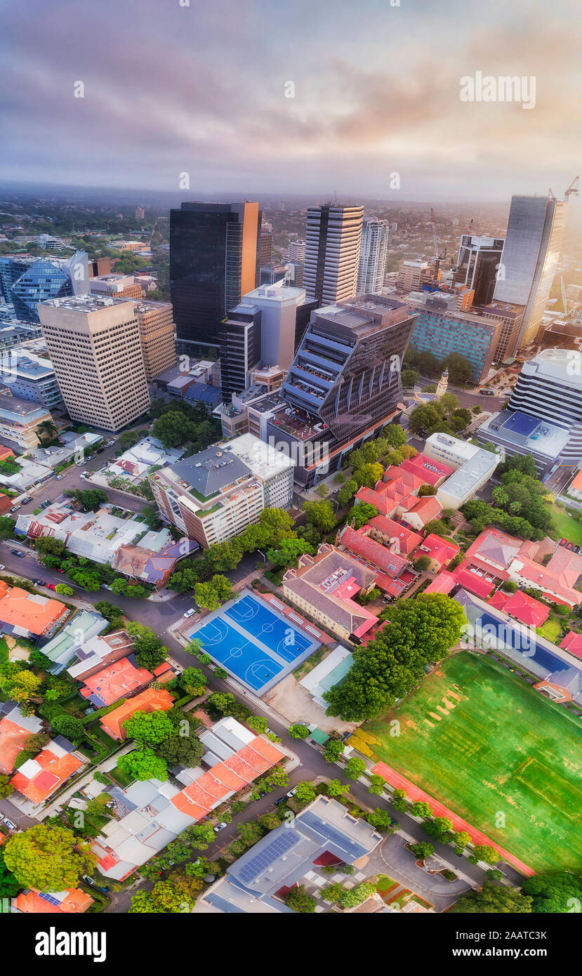 High-rise office towers in North Sydney CBD around historic post office building with school grounds of green lawn and sport courts - vertical aerial Stock Photo