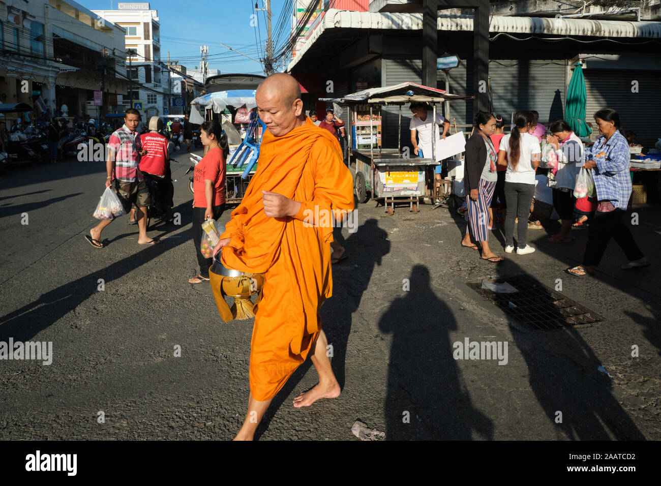 A Buddhist monk on his early morning alms round and carrying an alms bowl passes through the main market in Phuket Town, Phuket, Thailand Stock Photo