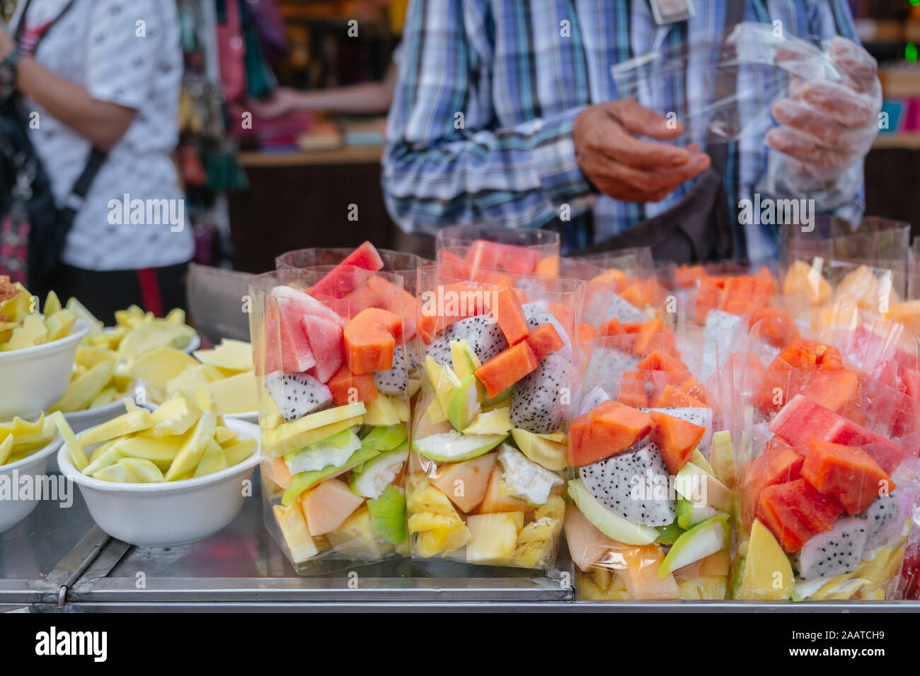 Various fresh tropical fruits in plastic bags and foam bowls for sale